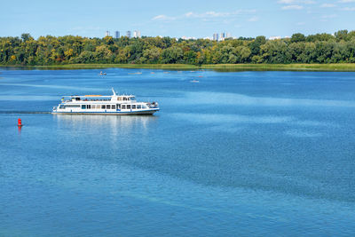 A pleasure boat goes along the green banks of the dnipro along the blue surface of the river on day.