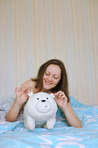 Smiling woman embracing stuffed toy sitting on bed at home