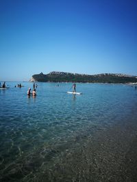 People in sea against clear blue sky