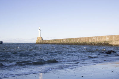 Lighthouse by sea against clear sky during winter