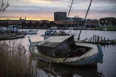 Fishing boats moored at harbor against sky during sunset