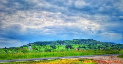 Road passing through field against cloudy sky