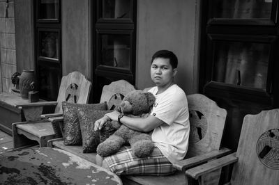 Portrait of man with teddy bear sitting on chair