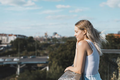 Side view of young woman standing against sky