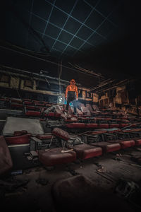 Digital composite image of man wearing mask while standing on broken chair in abandoned movie theater