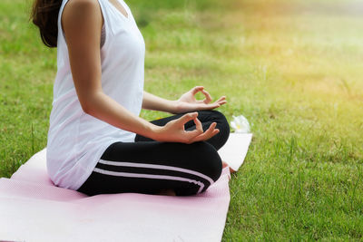 Low section of woman doing yoga while sitting on field