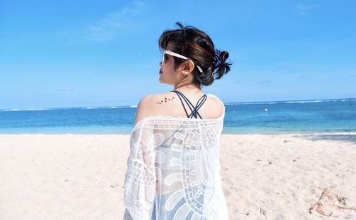 Rear view of young woman standing at beach against sky