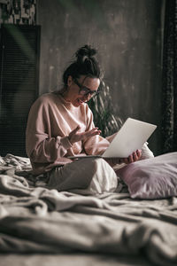 Midsection of woman sitting on bed at home