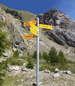 Road sign by rocky mountains against sky