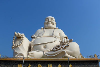 Low angle view of giant laughing buddha against clear blue sky
