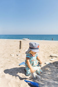 Boy sitting on sand at beach against clear sky