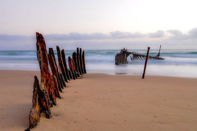 Wooden posts on beach against sky during sunset