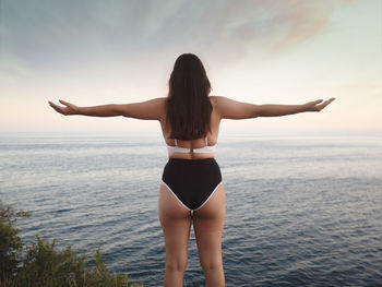 Rear view of woman jumping in sea against sky during sunset