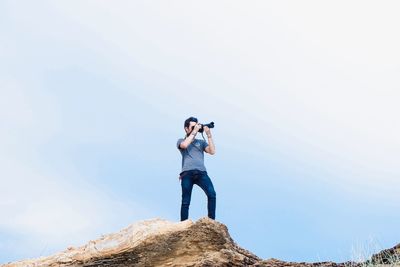 Low angle view of man photographing on mountain against clear sky