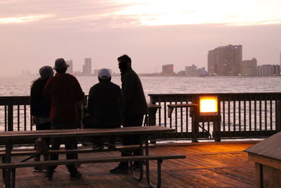 Rear view of people overlooking sea at sunset