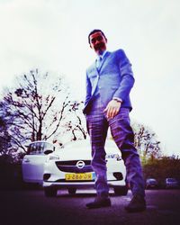 Man wearing sunglasses standing by car against sky