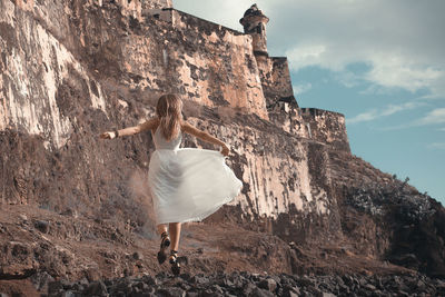 Rear view of woman standing on rock against sky