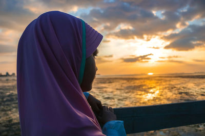 Girl looking at sea against sky during sunset