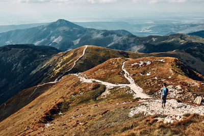 Young man with backpack hiking in a mountains, actively spending summer vacation