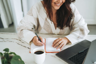 Smiling brunette woman with long hair in white cardigan working on laptop in office