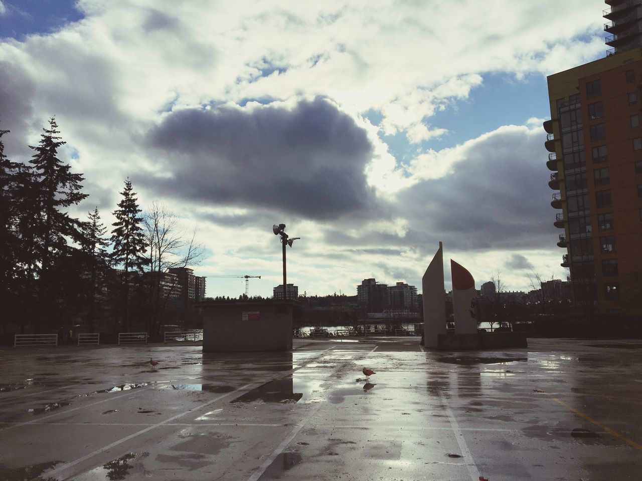 WET ROAD BY BUILDINGS AGAINST SKY