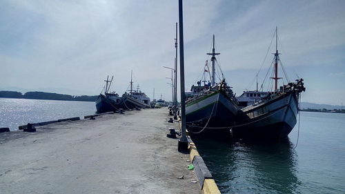 Fishing boats moored at harbor against sky