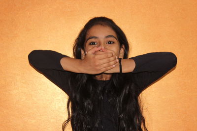 Portrait of teenage girl covering mouth against orange wall