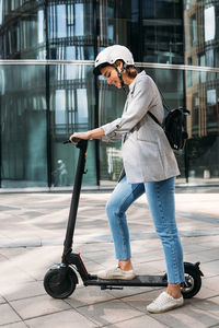 Young caucasian woman wearing cycling helmet standing outdoors with electric push scooter
