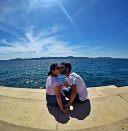 Man kissing woman while sitting on steps against sea