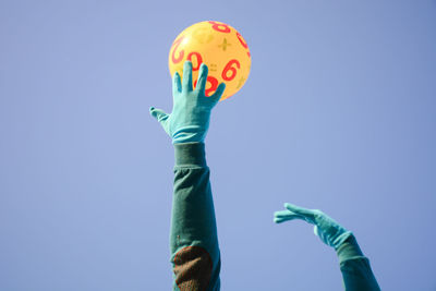 Low angle view of person catching yellow ball against blue background