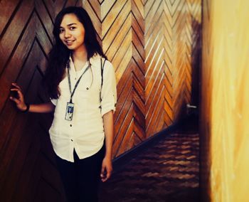 Portrait of smiling young woman standing by wooden wall