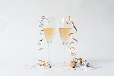 Two glasses of champagne, cork, ribbon and confetti on white backdrop.