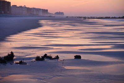 Beach by buildings against sky during sunset