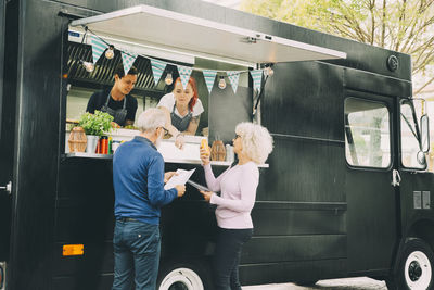 Smiling owners talking to senior customers while standing in commercial land vehicle