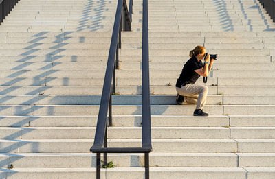 Side view of woman photographing on staircase