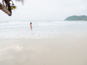 Hipster young woman in bikini walking barefoot on the beach and look to the little waves. 