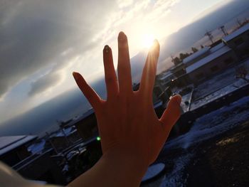 Close-up of hand against sky during sunset