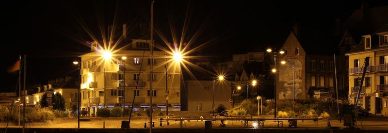 Illuminated buildings by street against sky at night