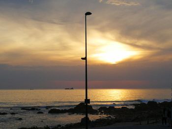 Silhouette street light on beach against sky during sunset