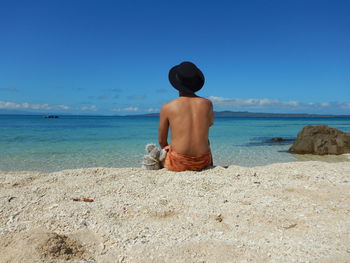 Rear view of shirtless man looking at sea against clear blue sky