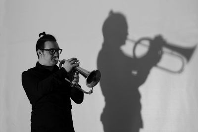 Musician playing trumpet by shadow on wall