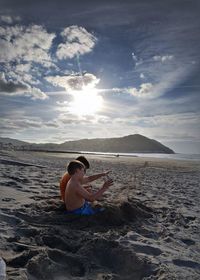 Boys sitting at beach against sky