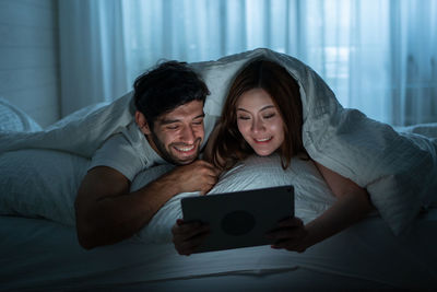 Man and woman using phone while standing on bed