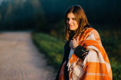 Portrait of smiling young woman with blanket standing on road