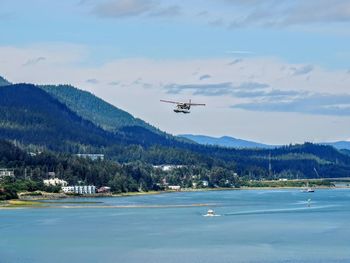 White float pontoon seaplane taking off from juneau harbor with boats and city in background