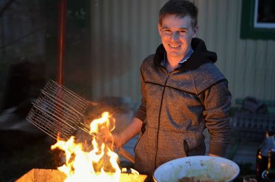 Portrait of smiling young man cooking food in yard at dusk
