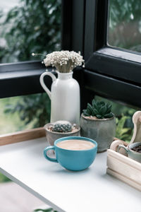 Close-up of coffee cup with potted plant on window sill
