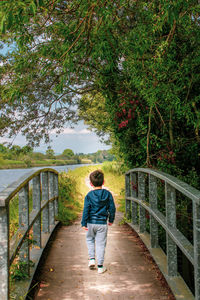 Full length rear view of boy walking on footbridge against trees