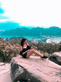 Young woman sitting on rock against mountains