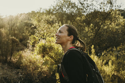 Side view of young woman looking away against trees